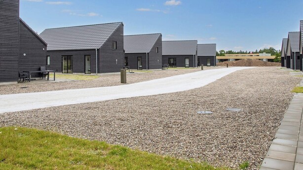 A row of modern, dark-colored buildings with sloped roofs, arranged in a linear fashion along a gravel path. - 5 Star Holiday Home in Romo (Rømø)