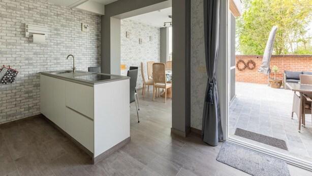 A modern kitchen with a central island, a dining area with a table and chairs, and a view of the outdoors through a sliding glass door. - Modern Villa w/ Private Yard (Middelkerke)