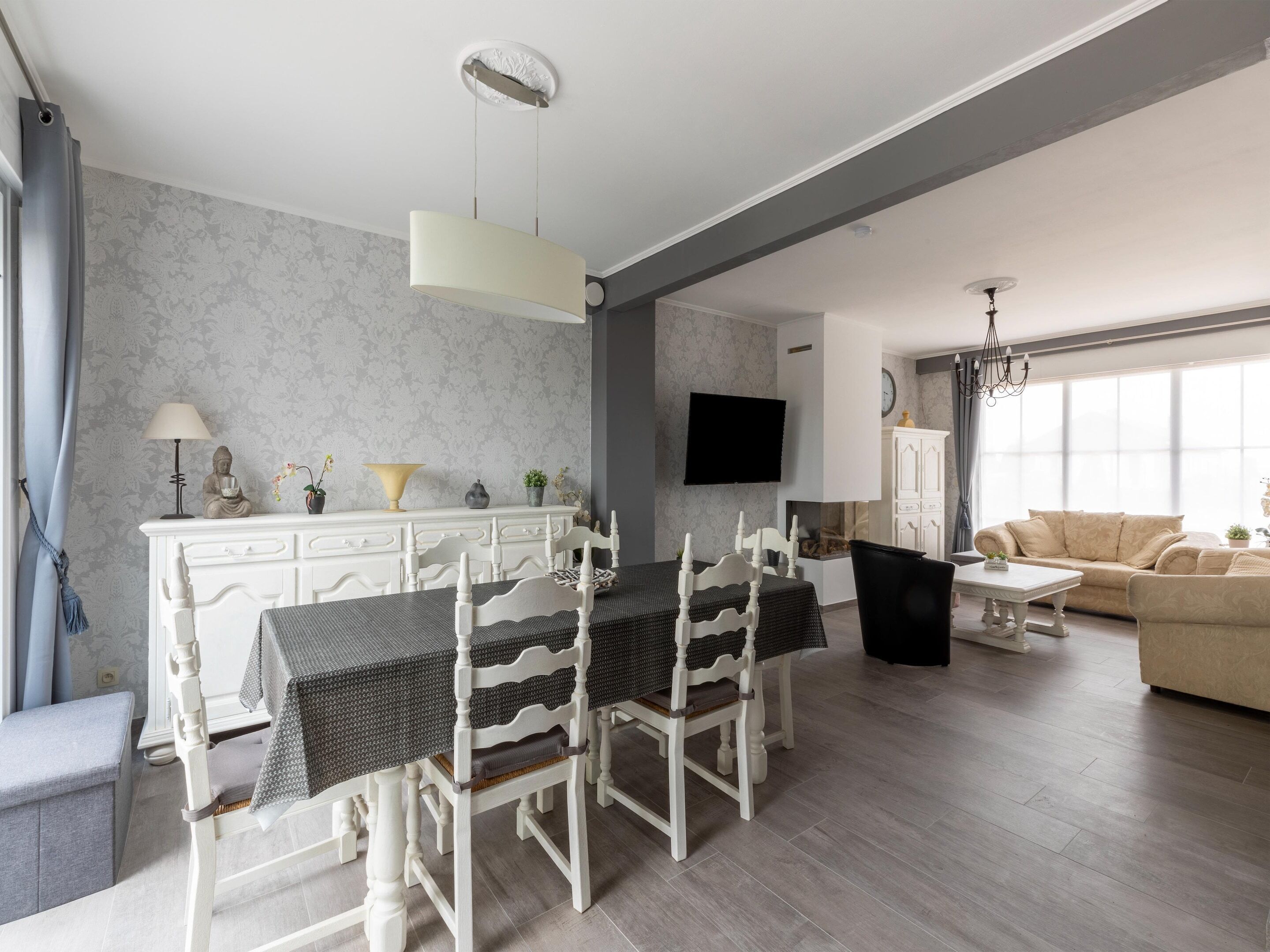 A modern living room with a dining area, a sofa, and a TV mounted on the wall.