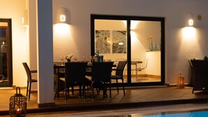 Un área de piscina interior con una mesa de comedor y sillas, una puerta de vidrio que da a una habitación y un cubo de basura pequeño.