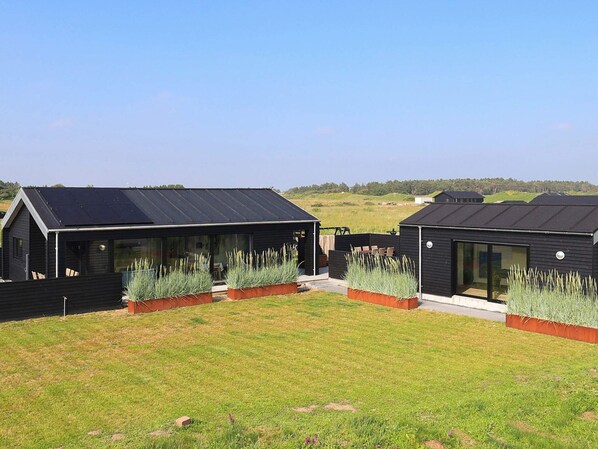Un bâtiment moderne doté d’un toit plat, de grandes fenêtres et d’une cour verdoyante avec des plantes.