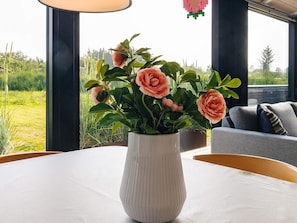 A white ribbed vase with flowers on a table, a window with a view of greenery, and a grey sofa with cushions. - 5 Star Holiday Home in Hirtshals (Hirtshals)