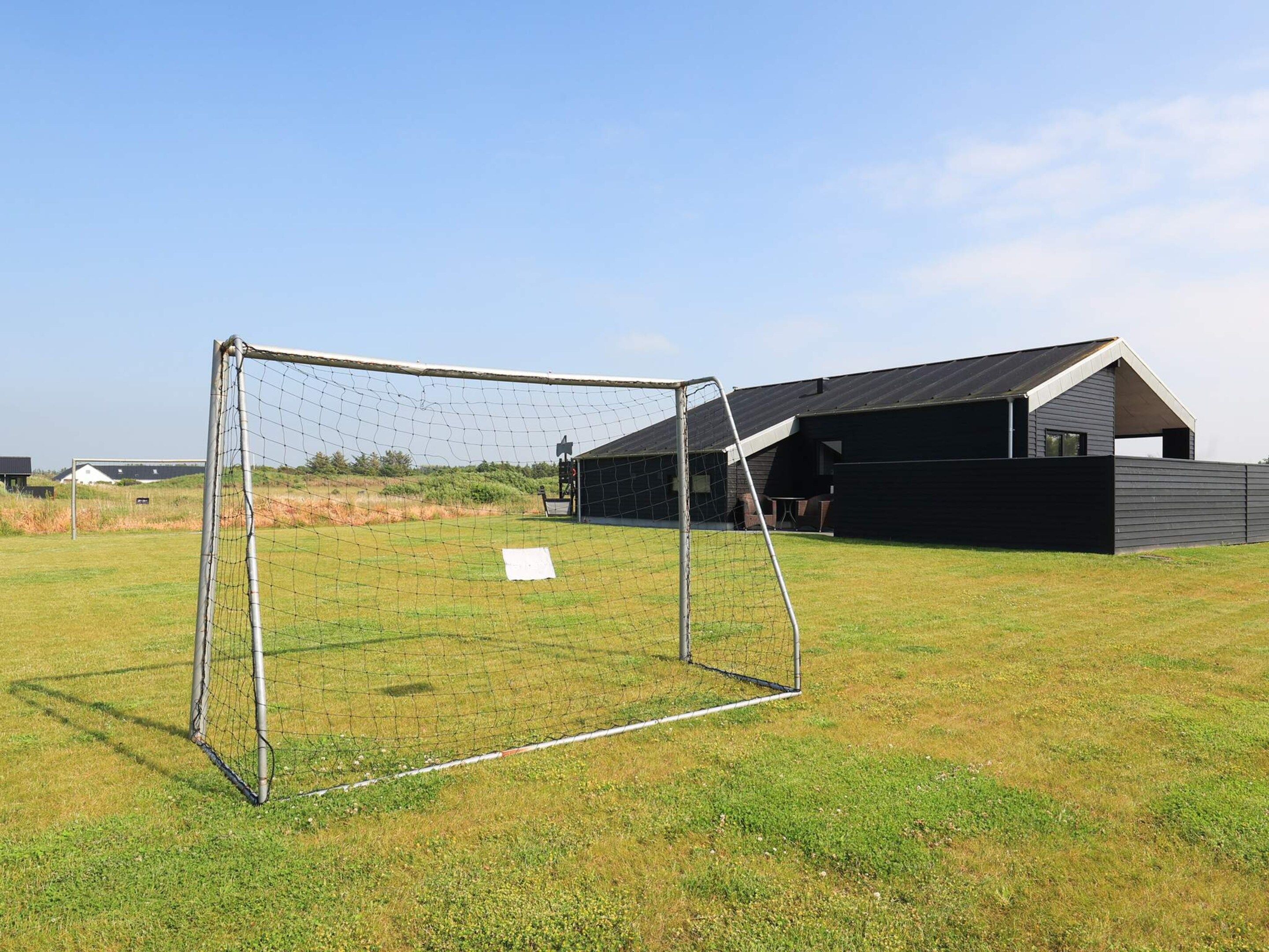 A soccer goal in a grassy field with a barn in the background.