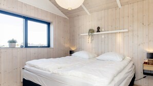 A bedroom with a bed, a window, wooden walls, and a shelf with a plant. - 5 Star Holiday Home in Hirtshals (Hirtshals)