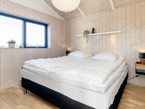 Une chambre à coucher avec un lit, une fenêtre, des murs en bois et une étagère sur laquelle est posée une plante.