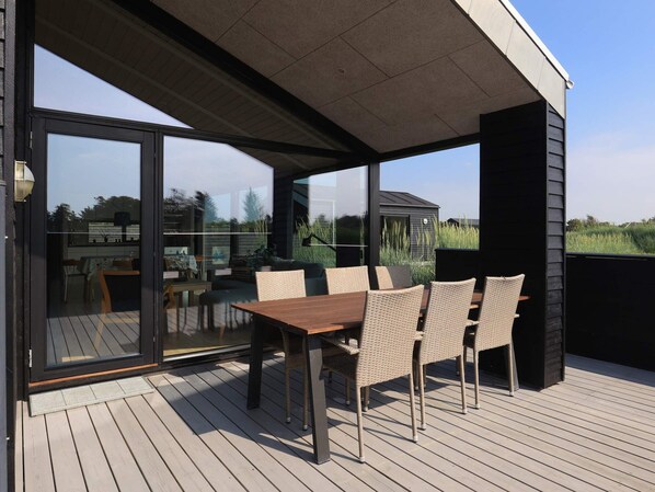 A covered outdoor seating area with a table and chairs, a sliding glass door, and a view of the surrounding landscape.
