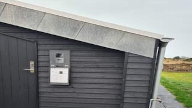 A dark wooden building with a metal door and a small electrical box mounted on the wall. - 5 Star Holiday Home in Hirtshals (Hirtshals)