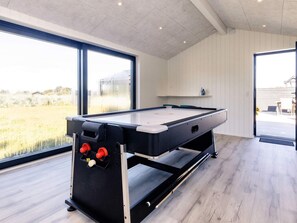 A pool table in a room with large windows, wooden flooring, and a ceiling with recessed lighting.