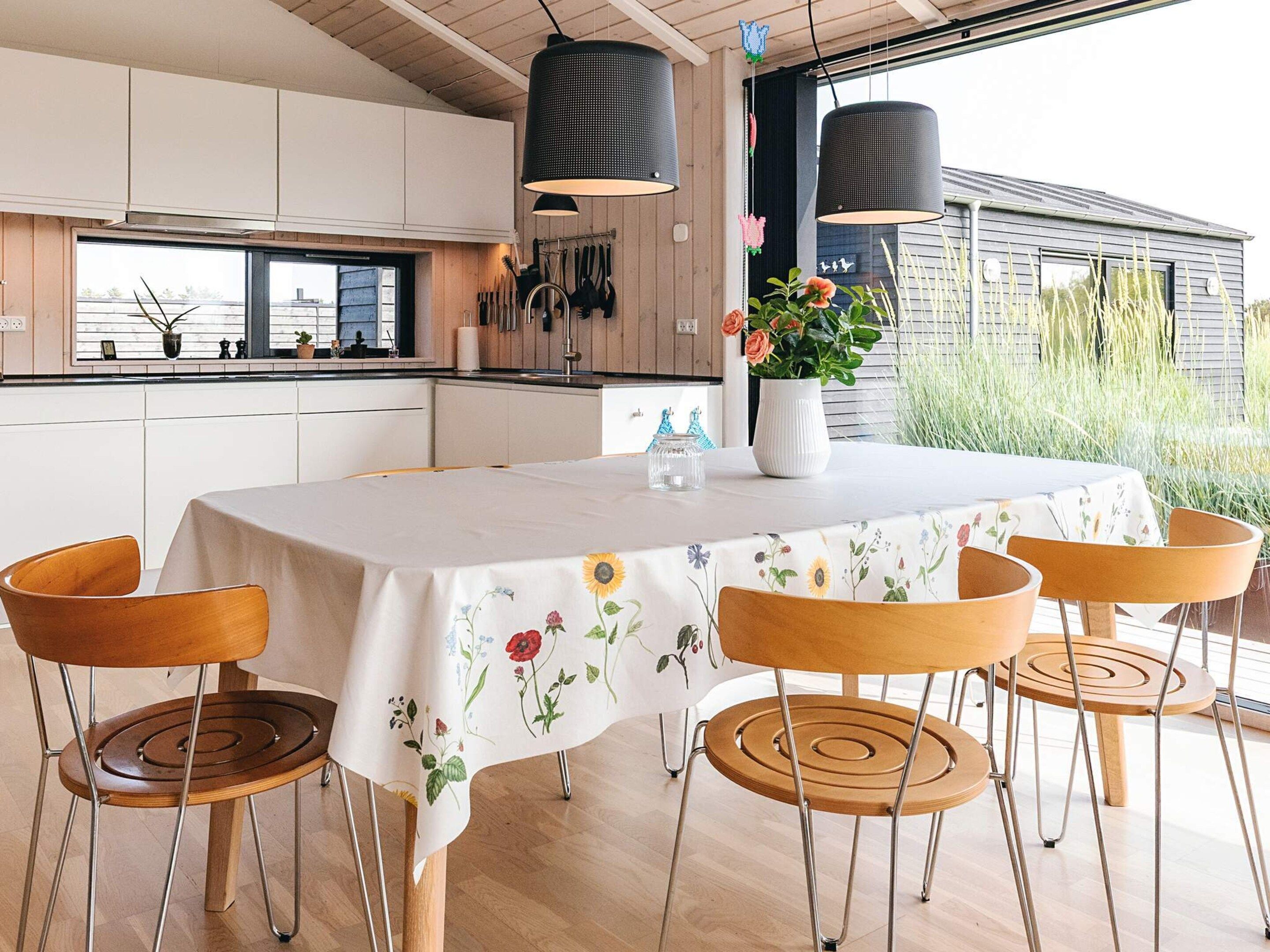 A modern kitchen with white cabinets, a dining table with a floral tablecloth, and a view of the outside.