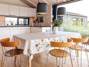 A modern kitchen with white cabinets, a dining table with a floral tablecloth, and a view of the outside. - 5 Star Holiday Home in Hirtshals (Hirtshals)