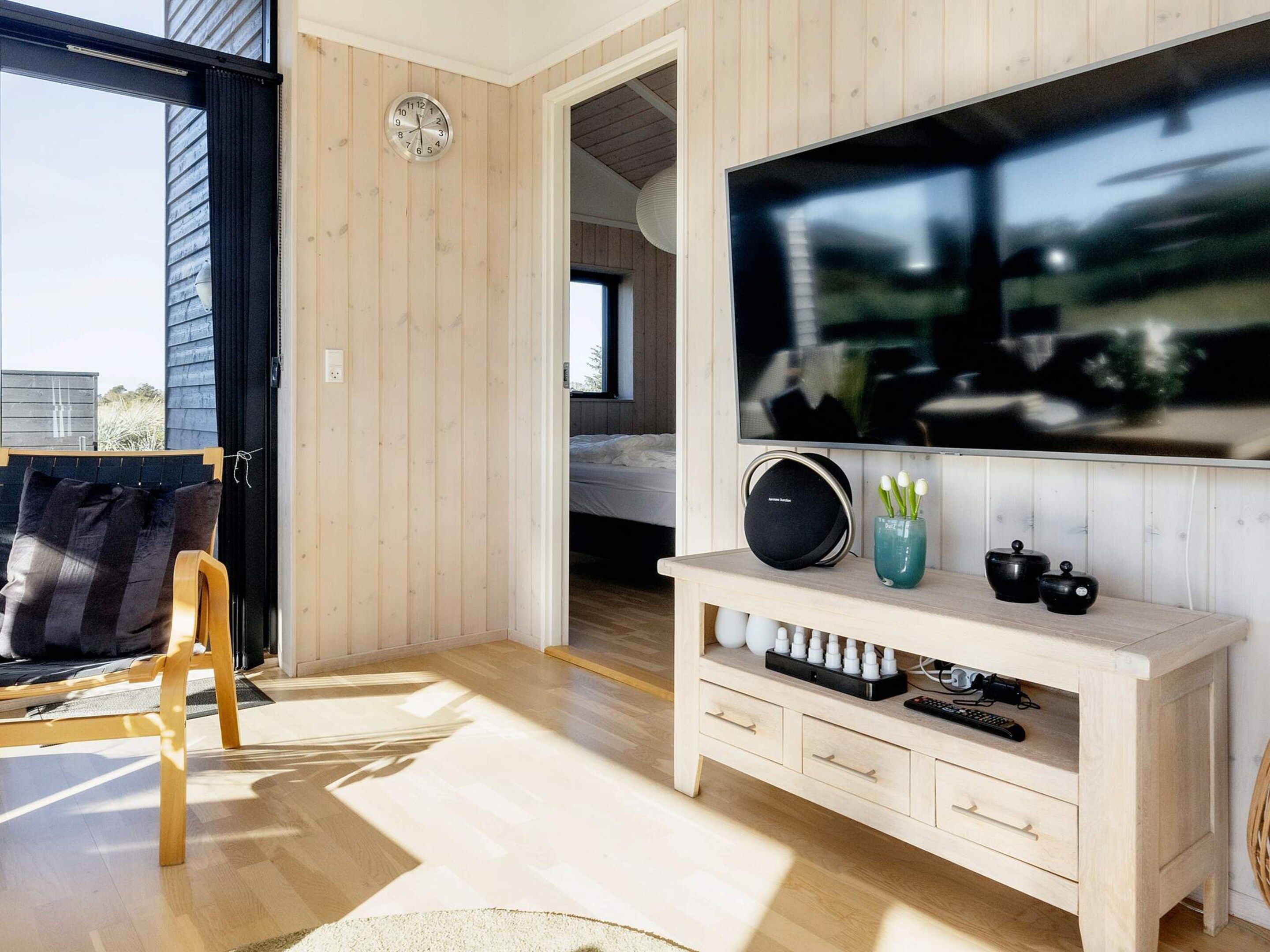 A modern living room with a large flat-screen TV, wooden flooring, a sofa, and a coffee table.