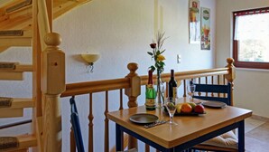 A dining area with a wooden table set for two, a vase with flowers, and a bottle of wine. - Apartment in Lancken-granitz (Lancken-Granitz)