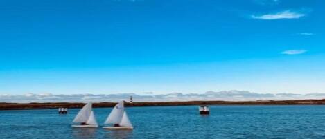 A calm lake with three sailboats and a lighthouse in the distance.
