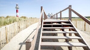 A wooden boardwalk leading to a lighthouse, with a sandy beach and grassy dunes on either side. - Apartment in Nieuwpoort Near Marina (Nieuwpoort)