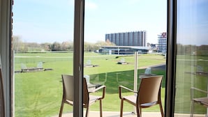 A balcony with two chairs and a table, overlooking a well-maintained lawn and a modern building in the distance. - Apartment in Nieuwpoort Near Marina (Nieuwpoort)