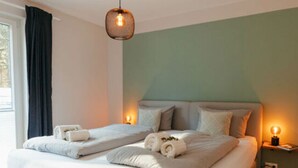 A modern bedroom with a large bed, a bedside table with a lamp, and a window with curtains. - Utkiek Stuuv Comfortable Holiday Residence (Ratzeburg)