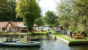 A canal with boats docked, a small building with a green roof, and a grassy area with tables and chairs. - Utkiek Stuuv Comfortable Holiday Residence (Ratzeburg)