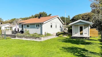A white house with a red roof, a small shed, and a well-maintained lawn.