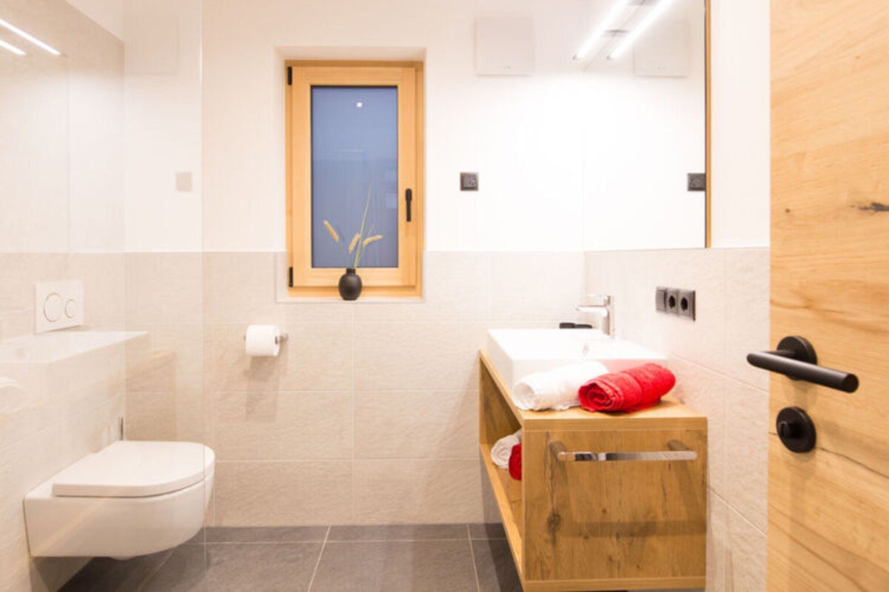 Un baño pequeño con inodoro, un tocador de madera con espejo y una ventana sobre el lavabo.