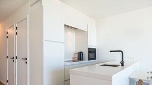 A modern kitchen with white cabinetry, a built-in oven, a coffee maker, and a black faucet.