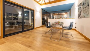 Un comedor moderno con una mesa y sillas de vidrio, techo de madera y vistas a otra habitación con mesa y sillas.