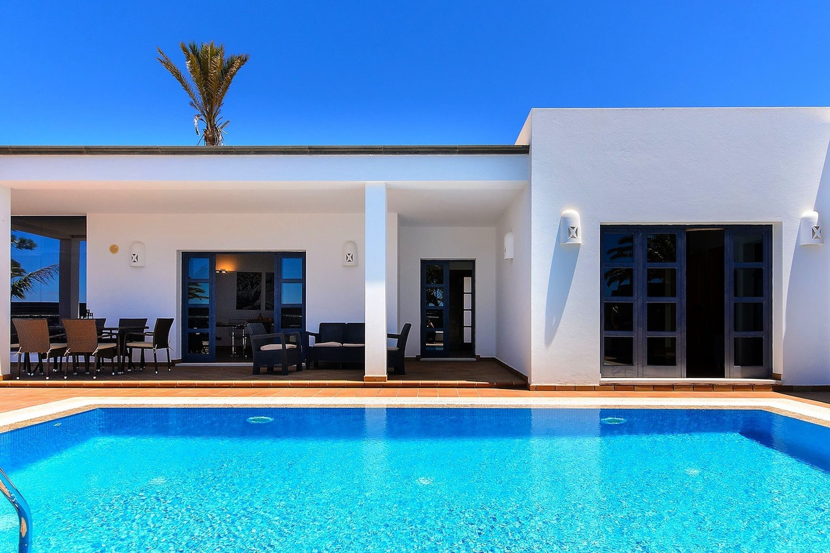 A modern poolside area with a clear blue pool, outdoor seating, and a white building facade.