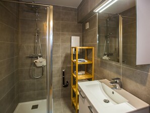 Een moderne badkamer met een douchecabine van glas, een witte wastafel en een houten schapunit.