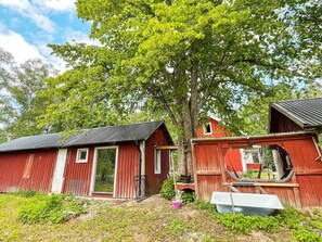 A red barn with a metal roof, a wooden structure with a window, and a tree in the background. - 4 Person Holiday Home in Furuby (Hovmantorp)