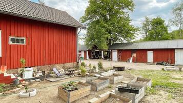 A red barn with a covered area, wooden raised garden beds, and a tree in the background.