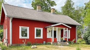 A red wooden house with a tiled roof, a porch, and a small garden area. - 4 Person Holiday Home in Furuby (Hovmantorp)