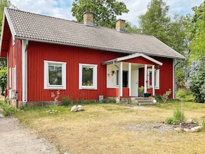 A red wooden house with a tiled roof, a porch, and a small garden area. - 4 Person Holiday Home in Furuby (Hovmantorp)