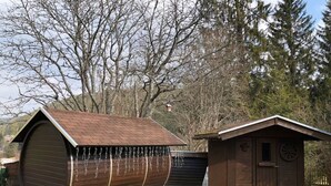 A wooden barrel-shaped building with a metal roof, a small wooden structure with a circular window, and a wooden fence in the background. - Kassler Comfortable Holiday Residence (Feldberg)