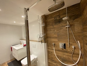 Ein modernes Badezimmer mit Duschkabine aus Glas, Holzpaneelen an der Wand und einem weißen Waschbecken.