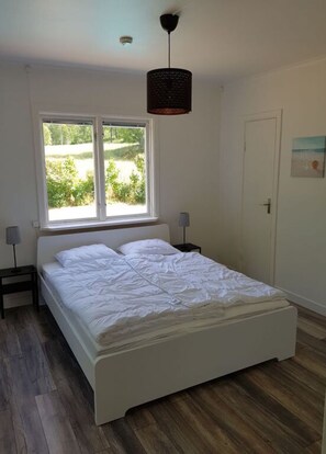Une chambre à coucher avec un lit, une fenêtre, une porte et un luminaire suspendu.