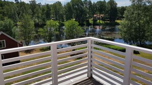 A wooden deck with white railings overlooking a lake surrounded by trees. - Country House Dalavagen 8 (Lönneberga)