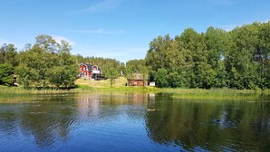 A serene lakeside property with a large red house and a smaller structure, surrounded by dense forest. - Country House Dalavagen 8 (Lönneberga)