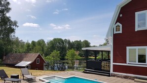 A swimming pool with lounge chairs, a covered patio, and a red building with a white window. - Country House Dalavagen 8 (Lönneberga)