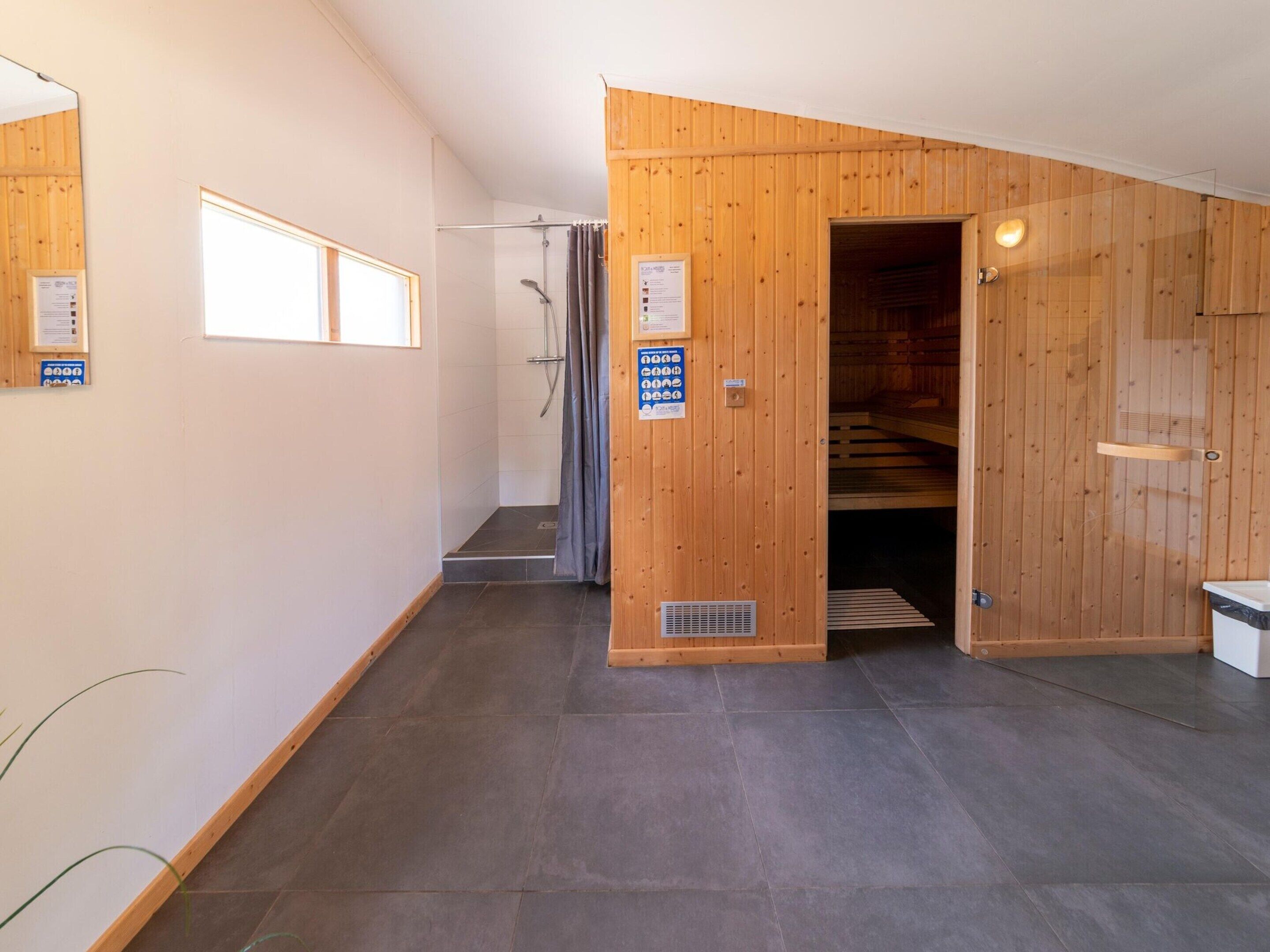A modern bathroom with a shower, a wooden wall, and a sign indicating amenities.