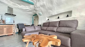 Een moderne woonkamer met een hoekbank, een houten salontafel en een keuken met een fornuis en kasten.