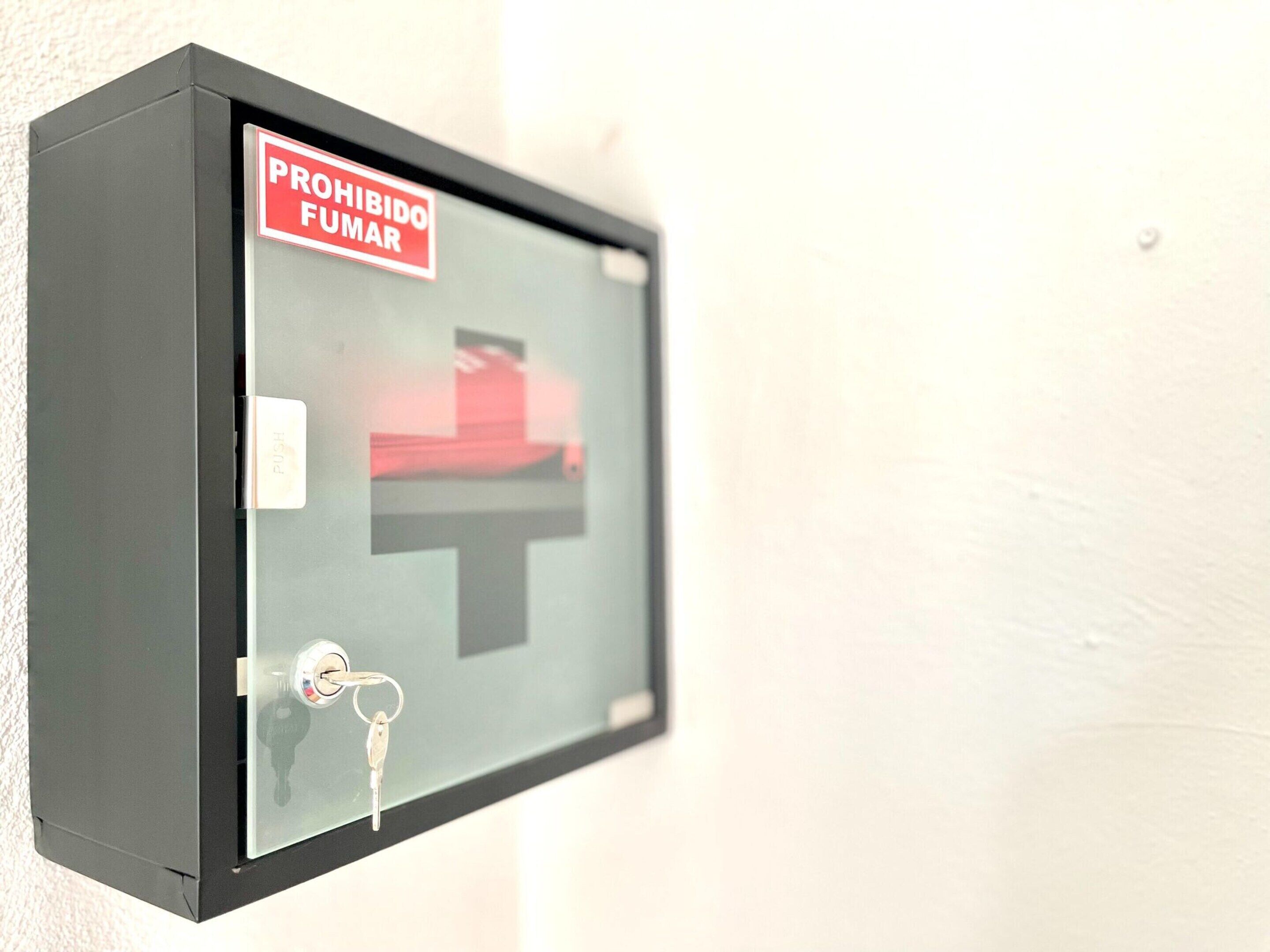 A black security box with a red sign that reads "PROHIBIDO FUMAR" (No Smoking).