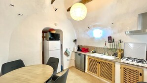 Een compacte keuken met een eethoek, met een houten tafel, stoelen, een inbouwfornuis en een hanglamp.