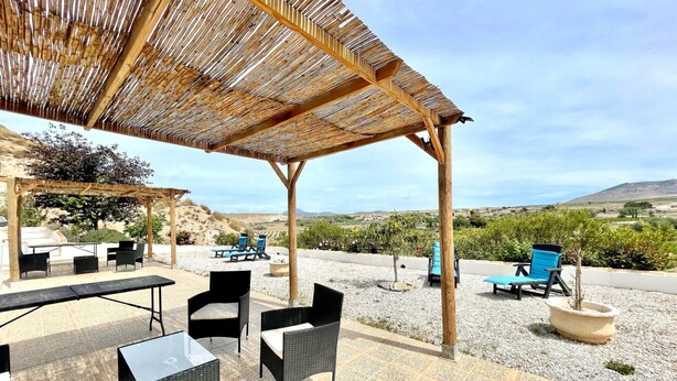 Een terras buiten met rieten meubilair, een pergola en uitzicht op het landschap.