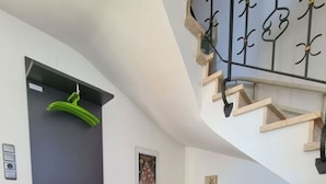 Una sala de estar moderna con un sofá gris, un cojín verde brillante, una escalera con barandilla de metal y una puerta con una toalla verde colgada.