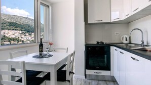 Una cocina moderna con armarios blancos, horno integrado y ventana con vistas a una colina.