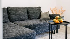 Una sala de estar moderna con un sofá seccional gris, una mesita redonda con un frutero y un jarrón con flores secas.