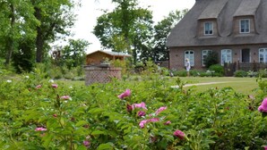 Una casa con fachada de ladrillo y tejado de paja, rodeada de un jardín con flores rosadas.