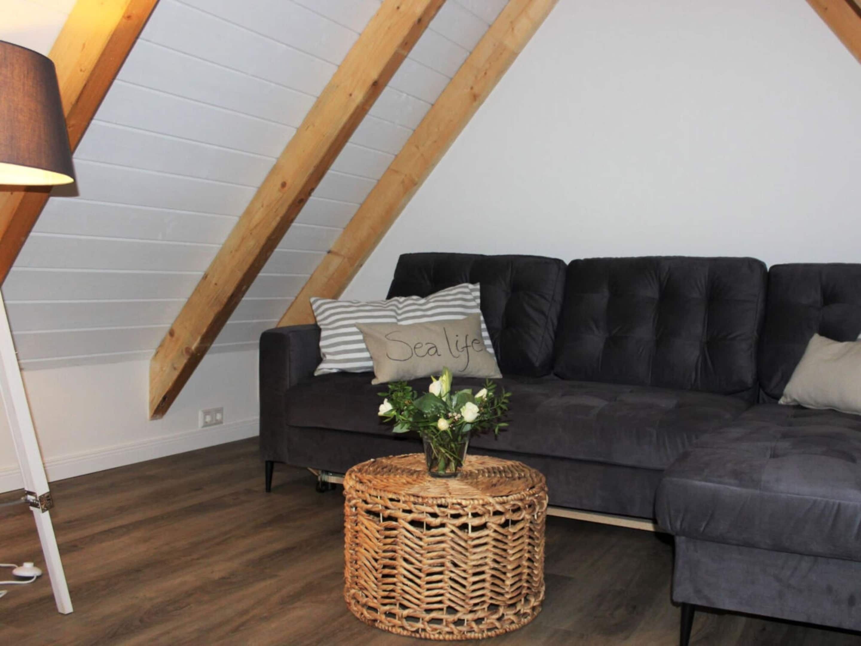 Un salon moderne avec un canapé gris foncé, une table d’appoint en osier et une lampe.
