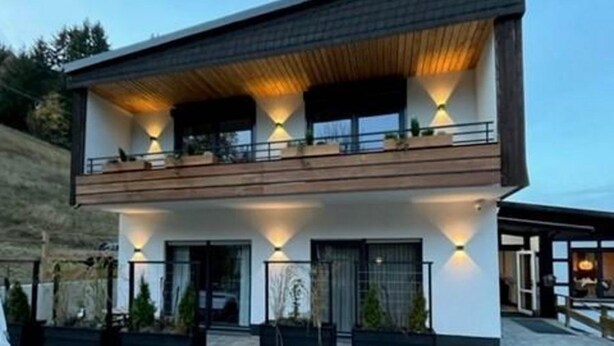 Una casa moderna de dos pisos con balcón, ventanas grandes e iluminación exterior.