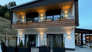 Una casa moderna de dos pisos con balcón, ventanas amplias e iluminación exterior.