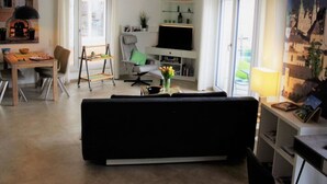 Uma sala de estar moderna com um sofá preto, uma mesa de jantar com cadeiras, uma televisão e uma estante de livros.